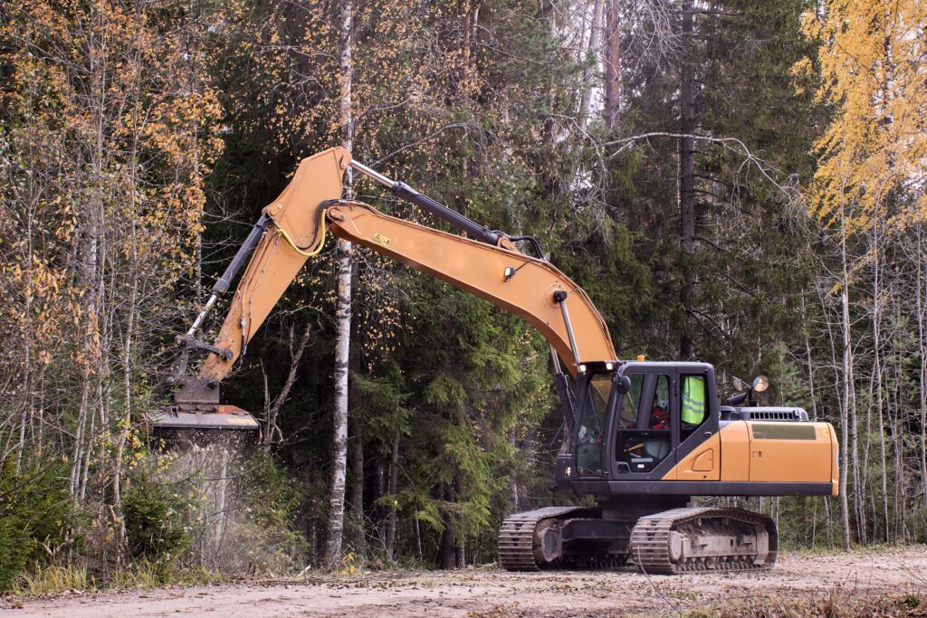 Forestry mulching machine attached to excavator, being used to clear roadside brush.
